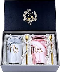 A "Mr. and Mrs." ceramic marble mug gift set nestled in a silver presentation box, featuring a gray marble mug, a pink marble mug, matching lids, and gold stirring spoons.