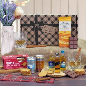 A curated gift hamper box arranged with miniature scotch whisky bottles, chocolate bars, ginger biscuits, mixers, and two glasses.