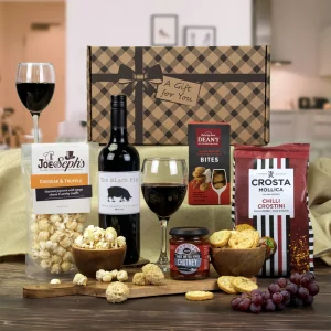 A luxury red wine, gourmet cheese bites, and savory snack gift hamper presentation.