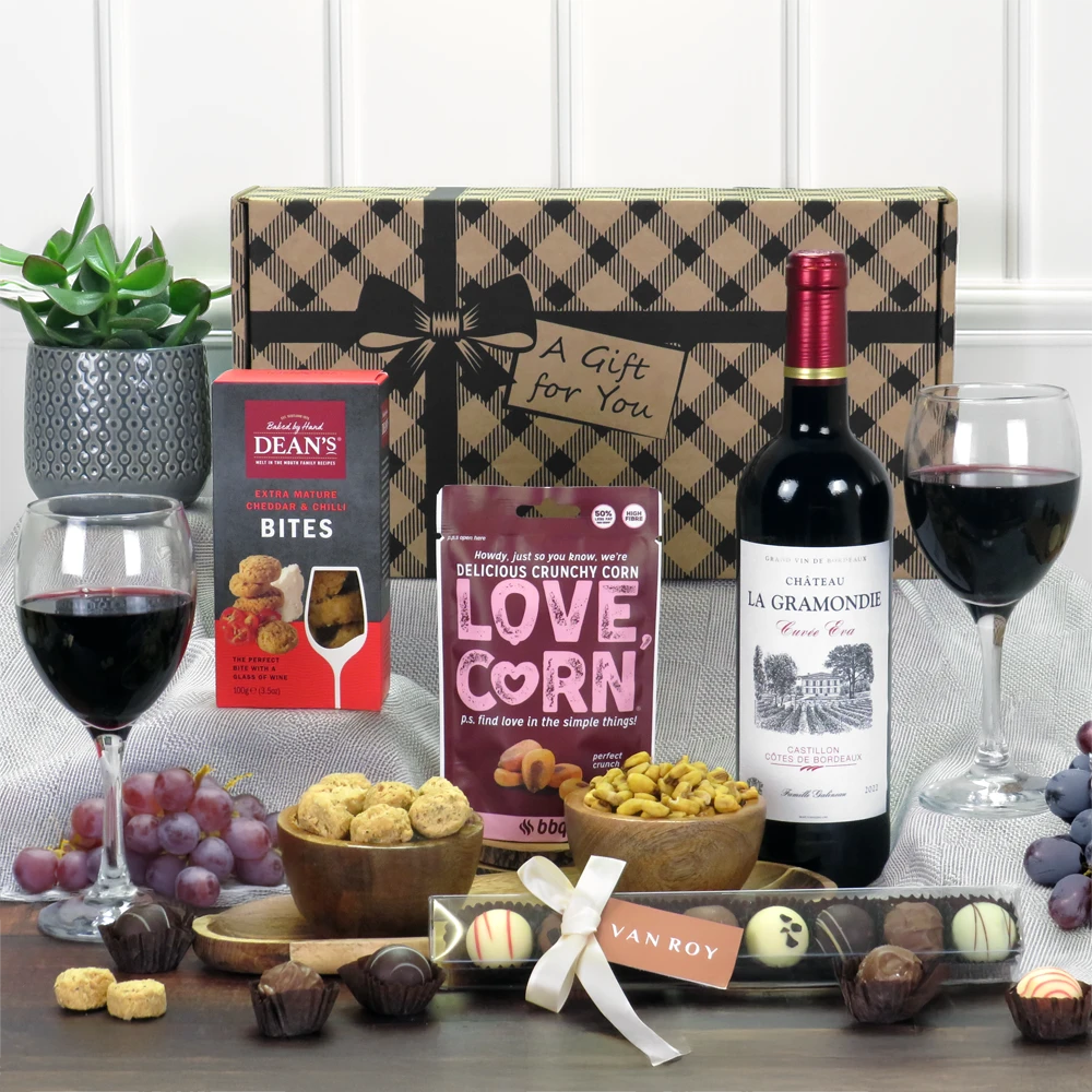 A premium Bordeaux red wine, luxury chocolate, and savory snack gift hamper presentation.