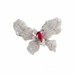 A Natkina Luminous Splash Butterfly Brooch featuring textured white silver wings encrusted with pavé-set diamond-imitation stones and a vibrant oval red ruby stamen at the center.