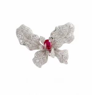 A Natkina Luminous Splash Butterfly Brooch featuring textured white silver wings encrusted with pavé-set diamond-imitation stones and a vibrant oval red ruby stamen at the center.