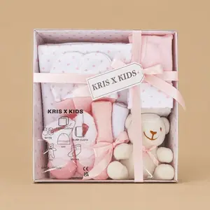 A pink and white "KRIS X KIDS" 7-piece newborn luxury gift set presented in a star-patterned display box tied with a pink ribbon and containing baby essentials alongside a small white plush teddy bear.