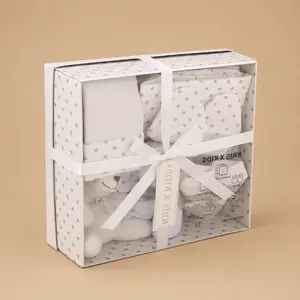 A neutral grey and white "KRIS X KIDS" 7-piece newborn luxury gift set presented in a star-patterned display box tied with a white ribbon, containing baby essentials and a small white plush teddy bear.