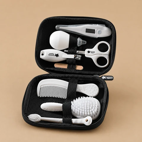 An open black zippered case containing a white Tommee Tippee baby healthcare and grooming kit against a light brown background.