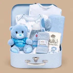 A baby boy gift hamper arranged inside an open light blue vintage suitcase, featuring a blue plush teddy bear, matching baby clothes, face cloths, and baby lotion.