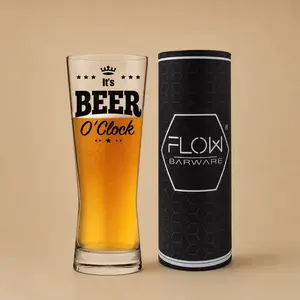A novelty "It's Beer O'Clock" craft ale glass filled with a cold drink alongside its stylized black presentation tube.