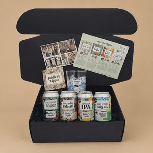 An open black gift box containing a variety pack of four Jiddler's Tipple craft beers with a matching printed glass, beer mat, and tasting guide on a solid beige background