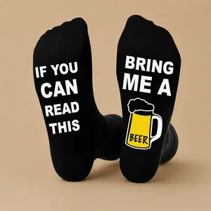 A pair of black novelty socks with funny message text on the soles reading "If you can read this, bring me a beer," ideal as a gift for beer lovers.