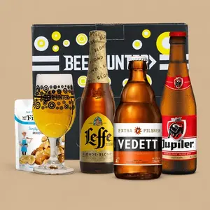 A Beerhunter Belgian Beer Gift Pack featuring three distinct bottles, a branded glass filled with beer, and a snack packet in front of a presentation box.