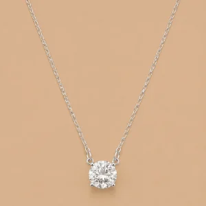 Minimalist silver solitaire necklace with a large round-cut sparkling crystal pendant centered on a plain light brown background.