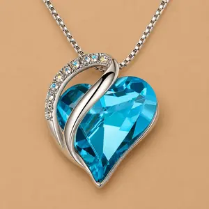 Sterling silver infinity heart pendant necklace featuring a brilliant, faceted aqua blue birthstone crystal. The heart silhouette is accented by a polished silver wave embedded with small round clear gems, suspended over a warm beige background.