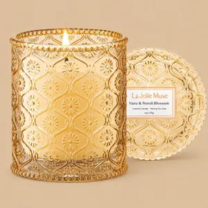 A lit "La Jolie Muse Yuzu & Neroli Blossom" glass jar candle with its lid.