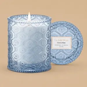 A lit "La Jolie Muse Citrus Mint" blue glass jar candle with its lid.