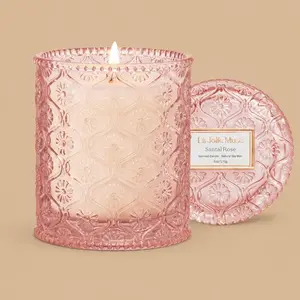 A lit "La Jolie Muse Santal Rosé" pink glass jar candle with its lid.