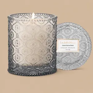 A lit "La Jolie Muse Linen Cotton Oasis" grey glass jar candle with its lid.