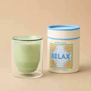 An Oliver Bonas Relax double-walled green jar candle next to its cylindrical packaging.
