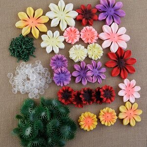 An organized layout of colorful faux flower petals, green plastic calyxes, flower centers, and plastic connectors on a textured brown surface.