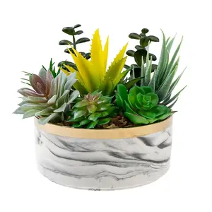 An arrangement of various faux succulents planted with small pebbles inside a round marble-patterned pot with a gold rim.