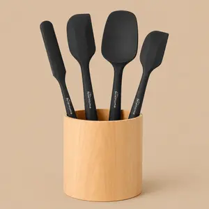 Modern black silicone baking spatula kit resting in a cylindrical wooden container against a uniform soft tan backdrop.