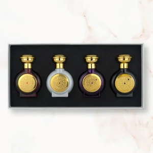 "An open rectangular gift box displaying four miniature, rounded Boadicea the Victorious perfume bottles in dark red, white, dark purple, and black glass, each adorned with a matching gold cap and a finely detailed circular gold shield emblem."