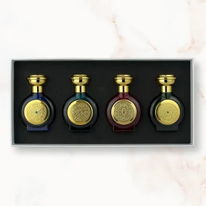 "An open rectangular gift box displaying four miniature, rounded Boadicea the Victorious perfume bottles in dark blue, teal, dark red, and dark green glass, each finished with a matching gold cap and a finely detailed circular gold shield emblem."