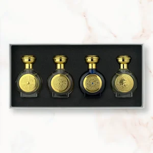 "An open rectangular gift box presenting four miniature, rounded Boadicea the Victorious perfume bottles in translucent olive yellow, clear glass, dark blue, and light translucent green, each styled with a heavy gold cap and a matching circular gold shield emblem."