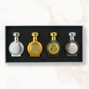 "An open rectangular gift box displaying four miniature, rounded Boadicea the Victorious perfume bottles: a metallic silver bottle, an all-gold bottle, a translucent olive-brown bottle with a gold shield, and a clear glass bottle filled with brown liquid featuring a silver shield."