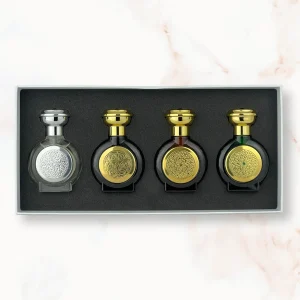 "An open rectangular gift box containing four miniature, rounded Boadicea the Victorious perfume bottles: a clear glass bottle with a silver cap and shield, followed by three dark glass bottles—black, dark burgundy, and forest green—each with golden caps and matching detailed shields."