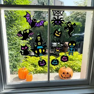 A window decorated for Halloween with colorful gel clings including a haunted house, ghosts, bats, and a skeleton, with three small pumpkins sitting on the window sill.