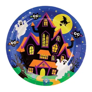 A round disposable paper plate featuring a vibrant Halloween illustration of a spooky haunted house with orange roofs, two cartoon ghosts, a full moon with a flying witch silhouette, and flying bats against a starry blue sky.