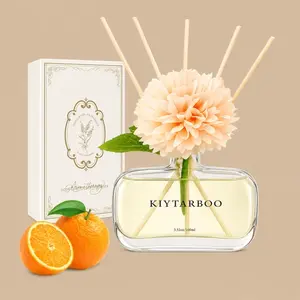 A KIYTARBOO reed diffuser set featuring an oval glass bottle topped with a large peach-colored faux flower, displayed alongside its white gift box and orange fruit accents.