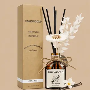 A GAGINGOOLD Vanilla Cream reed diffuser set featuring an amber glass bottle styled with a twine bow, black reeds, a large white faux flower, and dried botanicals next to its kraft paper gift box.