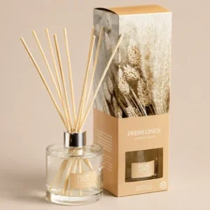 A Wax Lyrical Fresh Linen reed diffuser set featuring a clear glass bottle with light-colored wooden reeds and a kraft paper gift box decorated with an image of dried pampas grass
