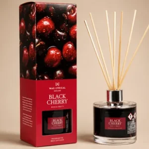 A Wax Lyrical Black Cherry reed diffuser set featuring a clear glass bottle filled with dark red liquid next to a gift box decorated with a photographic print of ripe cherries.