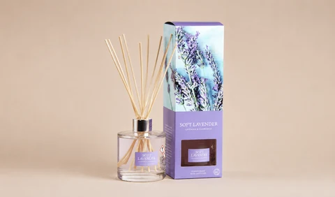 A Wax Lyrical Soft Lavender reed diffuser set featuring a clear glass bottle with light-colored wooden reeds and a pastel purple gift box decorated with an image of fresh lavender stems.