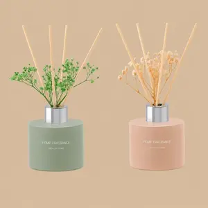 Two minimalist "Home Fragrance" reed diffusers—one matte green and one pastel pink—topped with wooden diffuser reeds and decorative dried botanicals.
