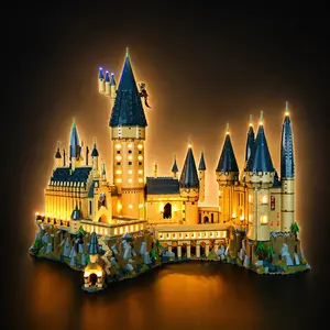 A completed LEGO Harry Potter Hogwarts Castle set fully illuminated with an aftermarket LED lighting kit, casting a warm yellow glow from the windows and towers against a black background.
