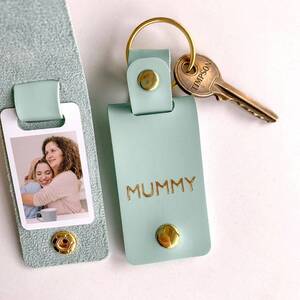 A mint green leather photo keyring with a gold split ring and key, debossed with the word "MUMMY" in gold foil, shown next to an unclasped section displaying a small color photograph of a mother and daughter.