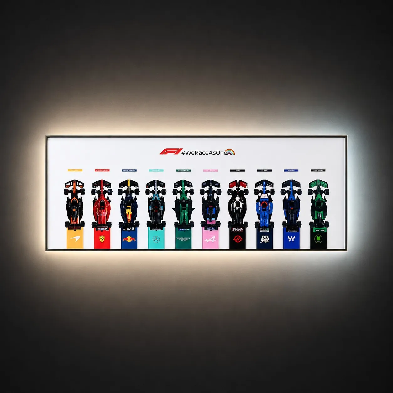 A horizontal, wall-mounted Brick Zone Hub White F1 10-Car Display Frame featuring an official red and black "#WeRaceAsOne" logo banner and ten brick-built race cars lined up side-by-side with bright white integrated ambient backlighting