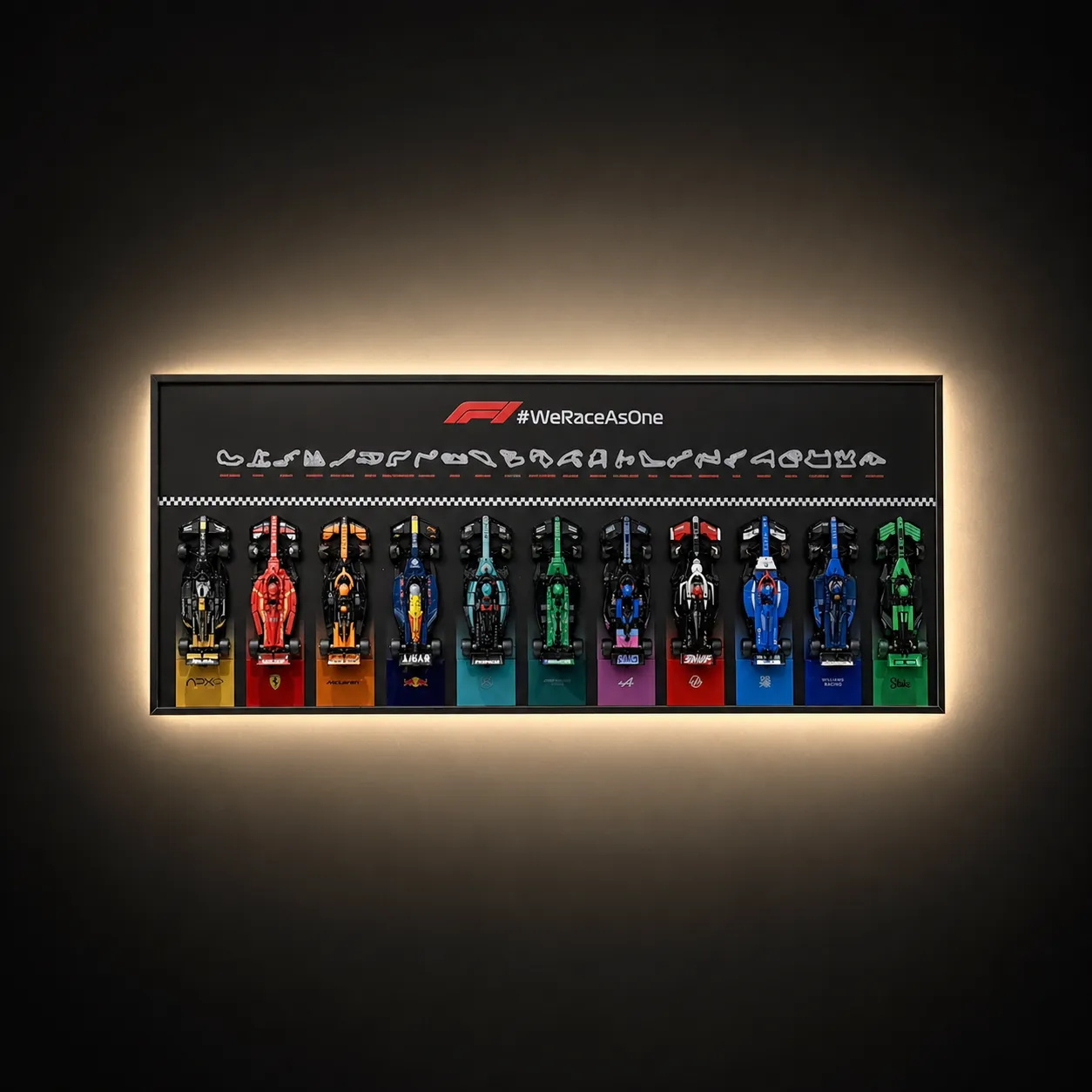 A horizontal, wall-mounted Brick Zone Hub F1 11-Car Display Frame featuring an official "#WeRaceAsOne" banner and 11 brick-built race cars lined up side-by-side with warm integrated ambient backlighting.