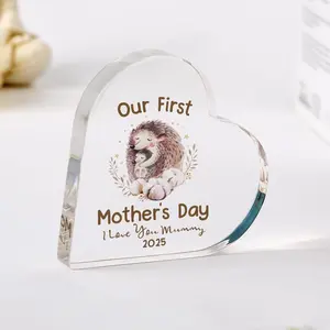 A clear acrylic, heart-shaped keepsake block featuring a cartoon illustration of two hugging hedgehogs and the text "Our First Mother's Day, I Love You Mummy 2025".