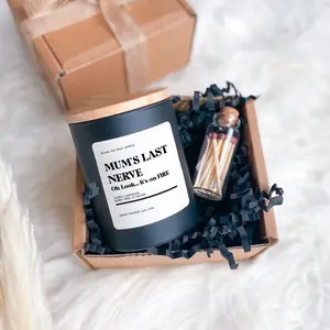 A funny Mother's Day gift box containing a matte black jar candle with a humorous label reading "Mum's Last Nerve: Oh Look... It's on FIRE", paired with a small glass jar of matches in black shredded paper packaging.