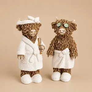 "Two textured brown Highland cow figurines dressed in white spa robes and slippers against a plain beige background."