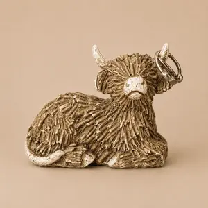 A rustic, twig-textured figurine of a resting Highland cow serving as a jewelry ring holder with two silver rings placed on its right horn.