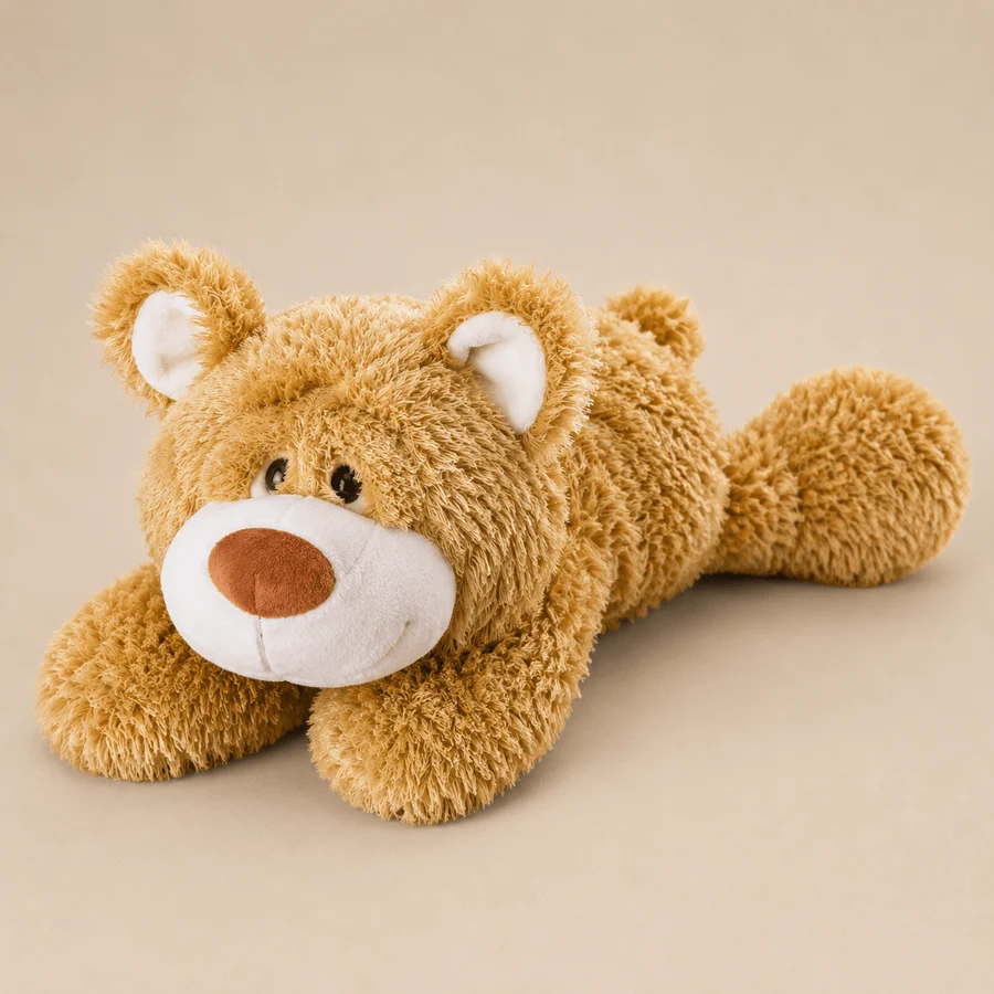 NICI classic plush teddy bear in a lying position. Features textured golden-brown shaggy fur, a contrasting white snout, a soft brown nose, and rounded ears over a matching tan backdrop.