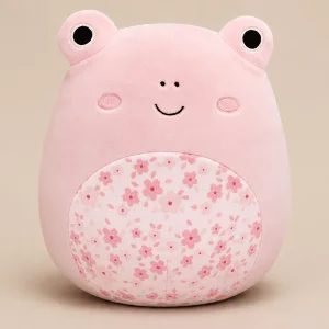 Kline the Pink Frog Squishmallow plush toy. Features a pastel pink body, minimalist embroidered smiley face, and a decorative cherry blossom floral patterned round belly panel on a plain beige backdrop.