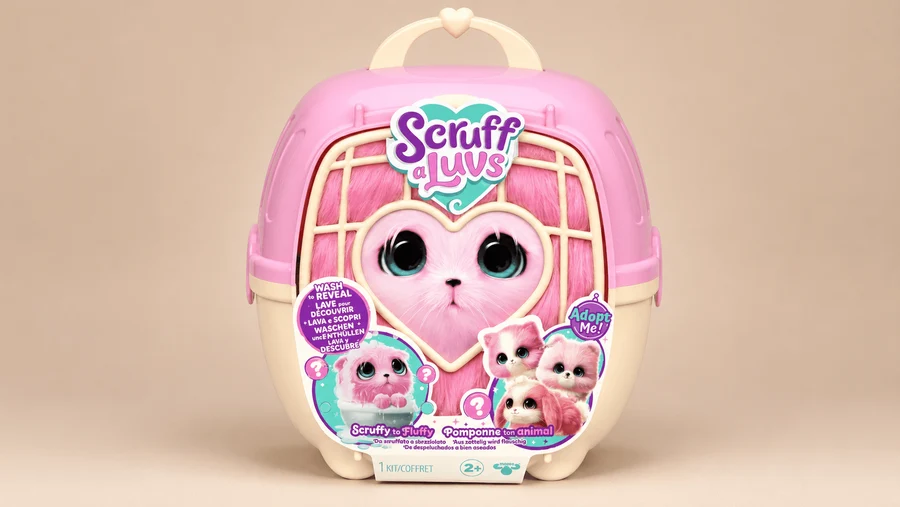 Scruff-a-Luvs Real Pets mystery surprise toy kit. Features a pink and cream pet carrier case with a heart-shaped window graphic showing an unwashed pink plush animal, accented by colorful multilingual stickers on a beige background.