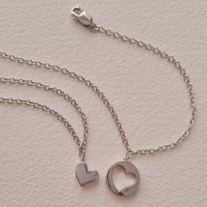 "A matching pair of 925 sterling silver chain bracelets from Hot Diamonds, featuring one bracelet with a small solid heart charm and the other with an open, circular heart-cutout charm, both accented with a single round-cut diamond."
