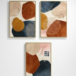 A set of three vertical thin-framed abstract paintings arranged with two on top and one centered below on a white wall, featuring organic shapes in terracotta, navy blue, ochre, and beige.